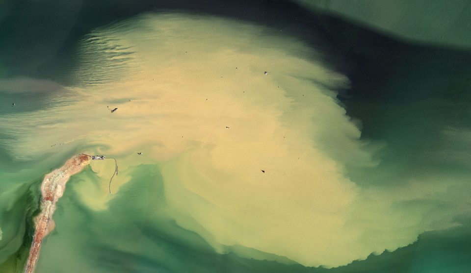 an aerial photograph showing an oil field facility. From this perspective the facility becomes abstract, with terrain resembling an abstract expressionist painting.