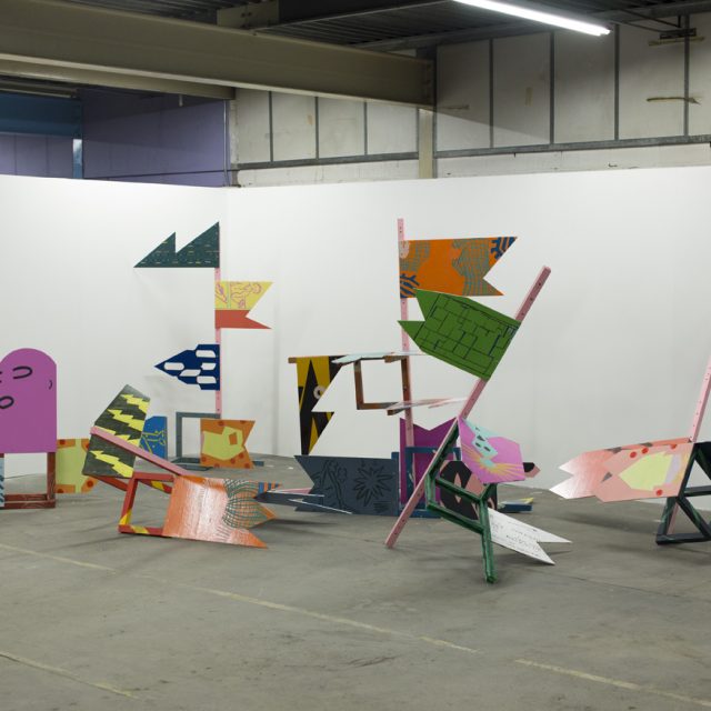 A photograph of an installation, made up of wooden poles and flag-shaped wooden panels