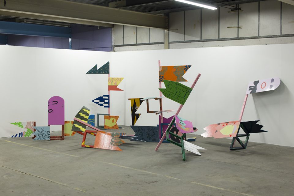 A photograph of an installation, made up of wooden poles and flag-shaped wooden panels