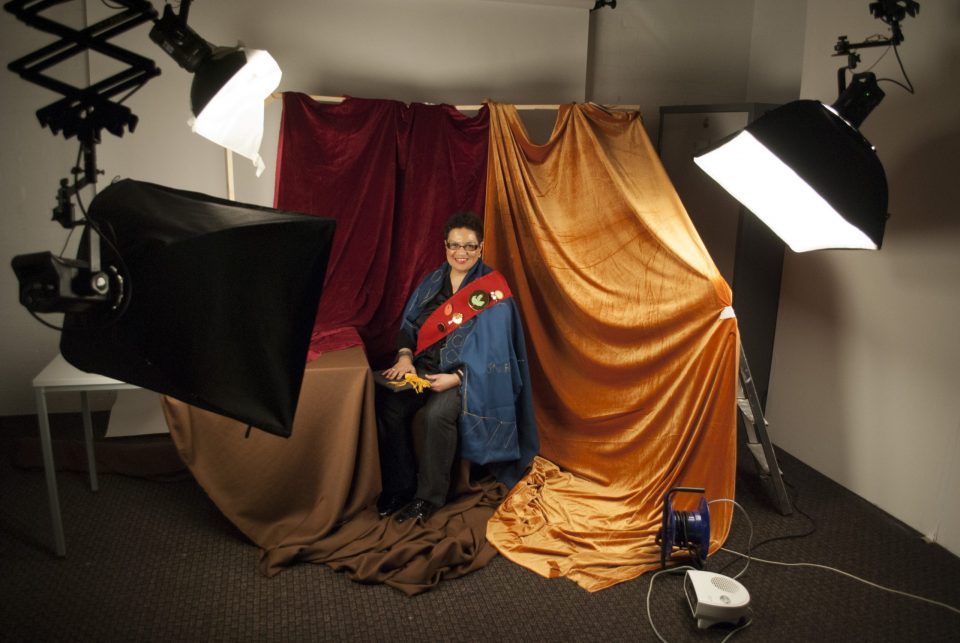 a photograph of Jackie Kay sitting for a portrait. The typical photographic studio equipment - lights, power cables and a heater - are all visible.
