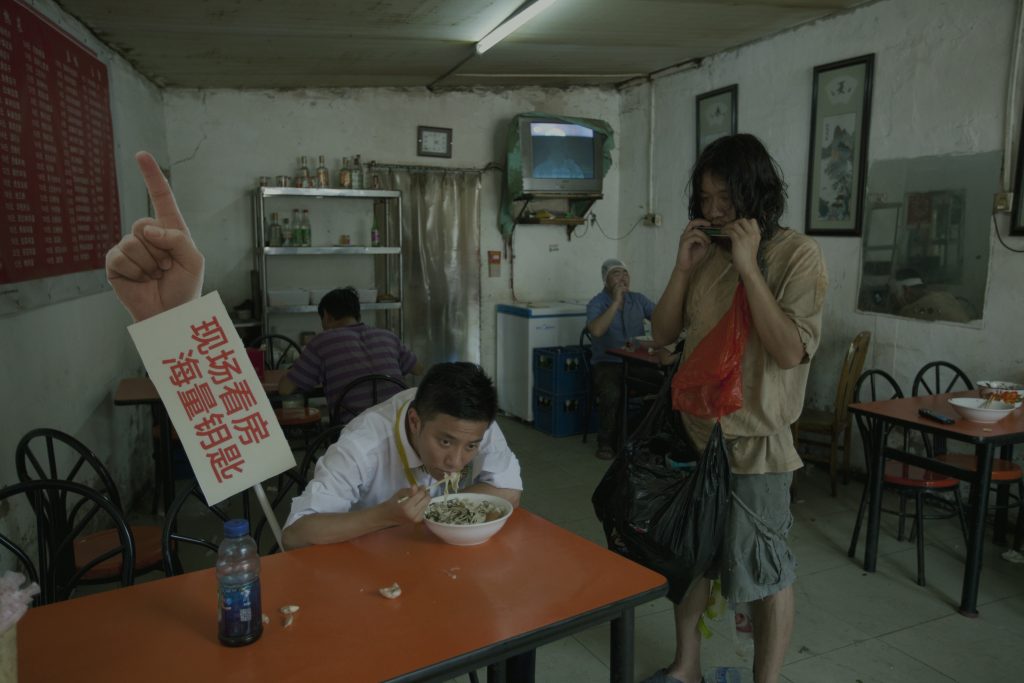 a film still showing two people in a dilapidated restaurant, one person is sitting eating and another is standing up