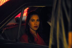 A film still, showing a woman looking out of a car window. From the lighting we can assume it is nightime