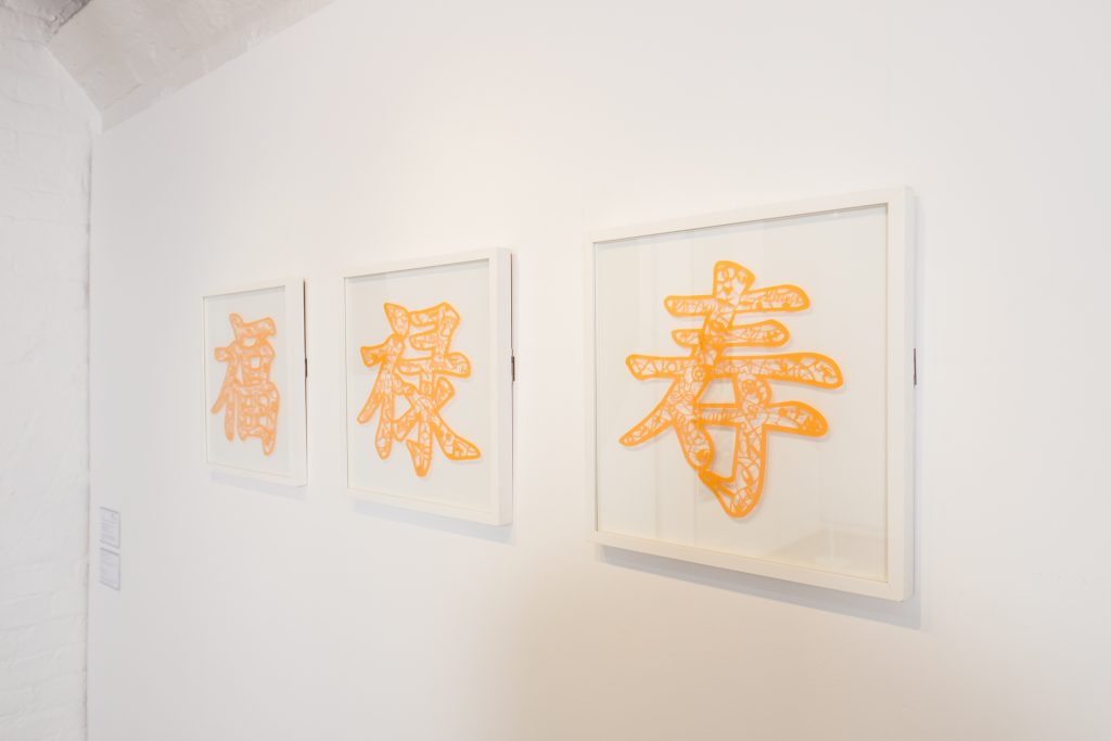 There are three orange paper-cut works on the picture, each with the Chinese characters Fu Lu Shou.