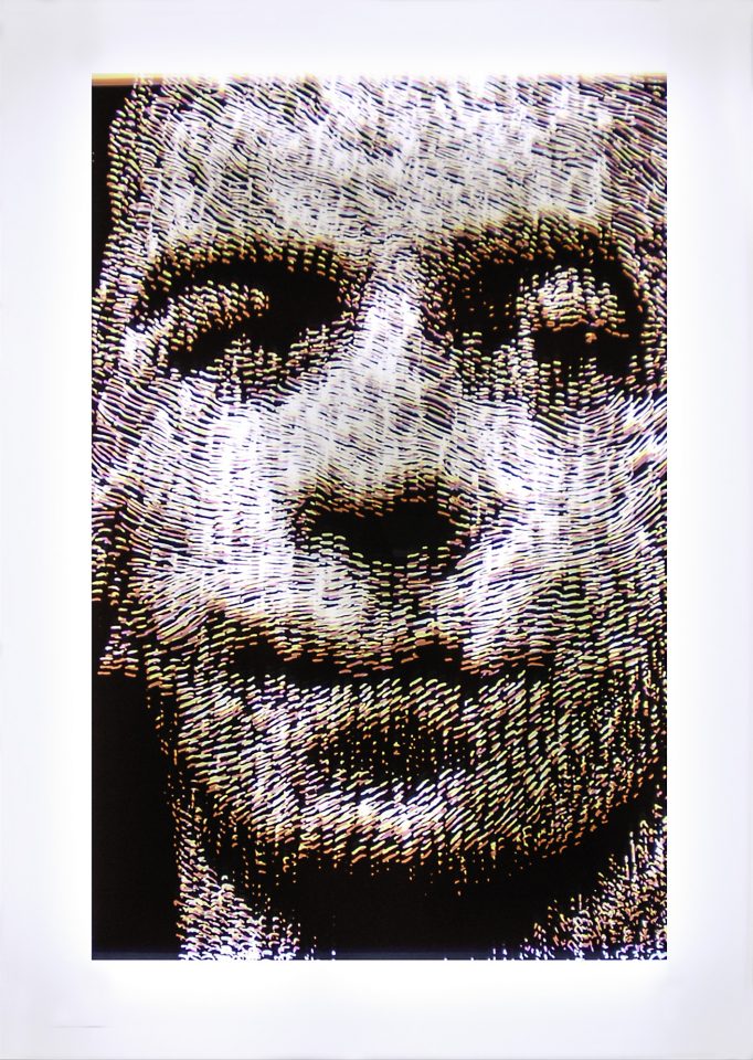 Layers of cyan, magenta, and yellow hand carved marks form the image of a mans face.