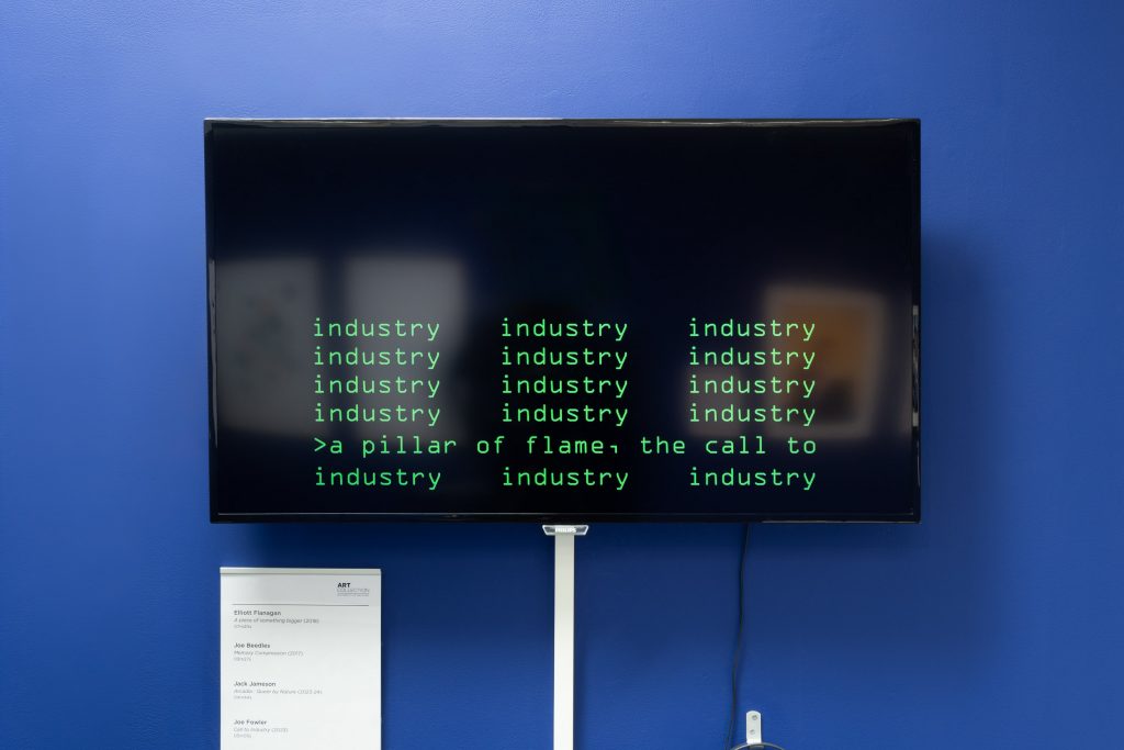 A large flat-screen television on a blue wall. The screen has green blocky text upon it, like you'd see in old movies where they hack computers - think the matrix. The screen reads: industry, a pillar of flame, the call to industry