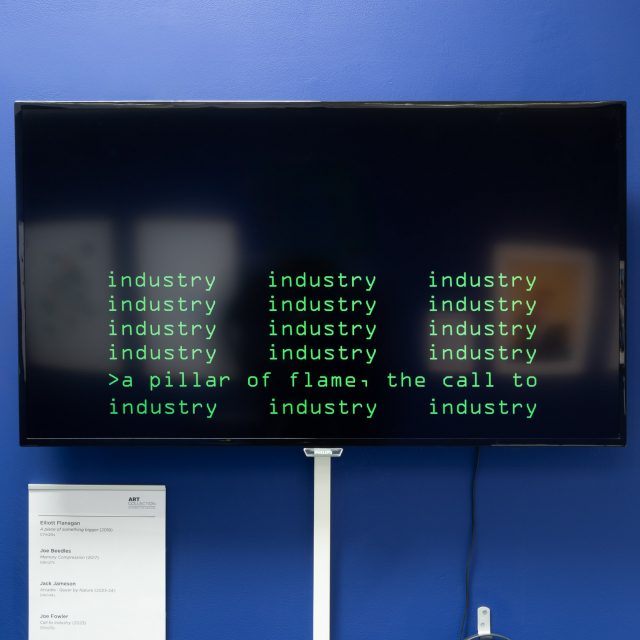 A large flat-screen television on a blue wall. The screen has green blocky text upon it, like you'd see in old movies where they hack computers - think the matrix. The screen reads: industry, a pillar of flame, the call to industry
